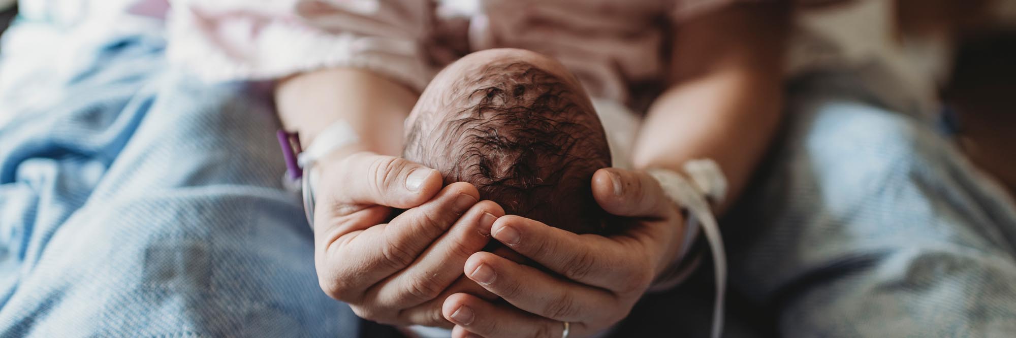 Hands gently cradling a newborn baby's head.