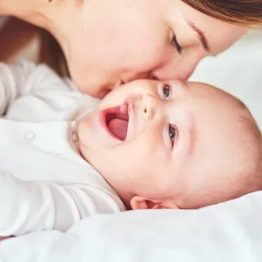 A mother lovingly kisses her smiling baby.
